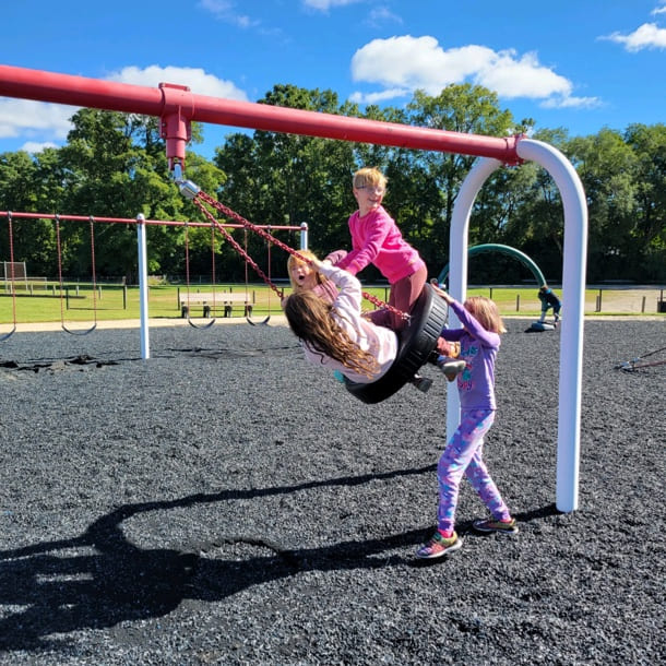 Three female students playing on a tire swing outdoors.