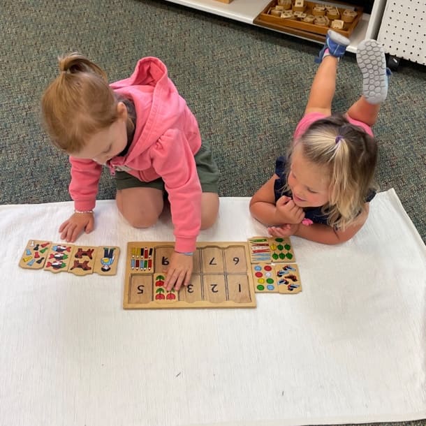 Two female students on the floor playing a matching game with tiles.
