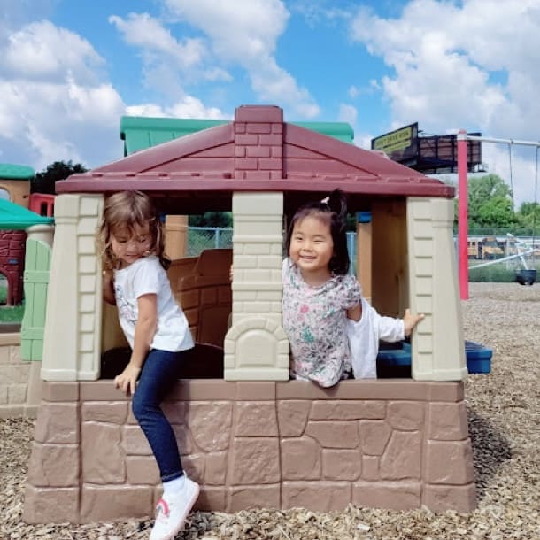 Two female students in the windows of a playhouse outdoors on the playground.
